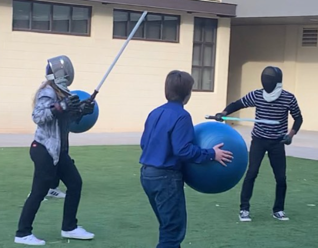 A fencing match begins while the combatants have to dodge a large blue Forceball flying in their direction.