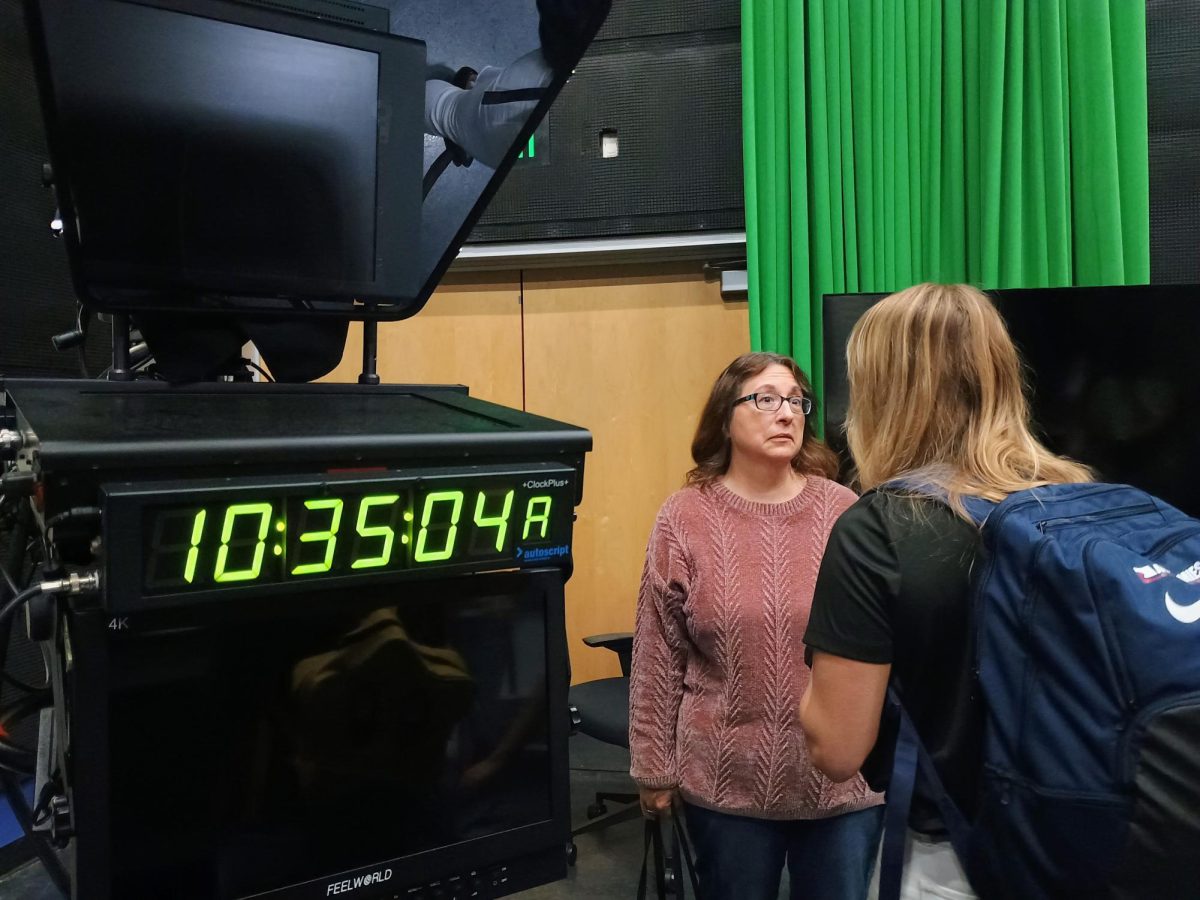 Mrs. Studts and Ms. May conversing near camera equipment in the news studio.